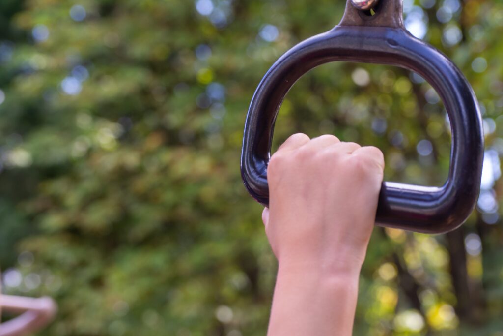 A woman's hand is holding a pull up bar in a park.