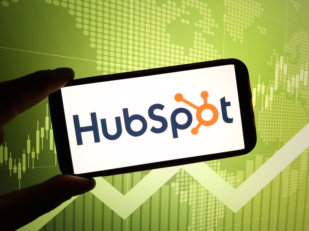 A person holding up a phone with the hubspot logo on it.