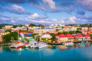 Colorful boats and buildings line the waterfront of a bustling coastal town under a cloudy blue sky.