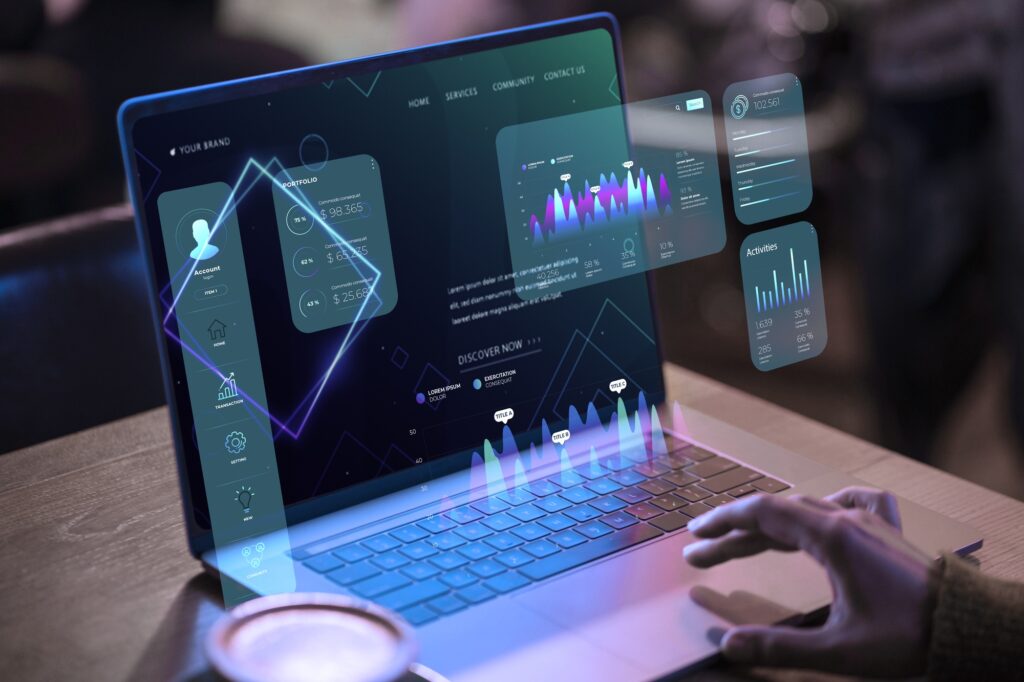 A person interacts with a laptop displaying holographic graphs and data visualizations, featuring bar charts and interface elements against a dark background.