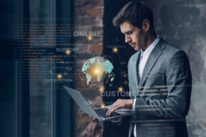 A man in a suit works on a laptop with digital graphics of a globe, code, and keywords like "ONLINE," "SUPPORT," and "CUSTOMER" overlaid, illustrating digital transformation for SMEs and business process automation.