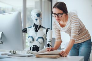 A woman reviews documents at a desk beside a humanoid robot, both examining papers and a computer monitor in a modern office—demonstrating how Agentic AI for SMEs streamlines everyday business tasks.