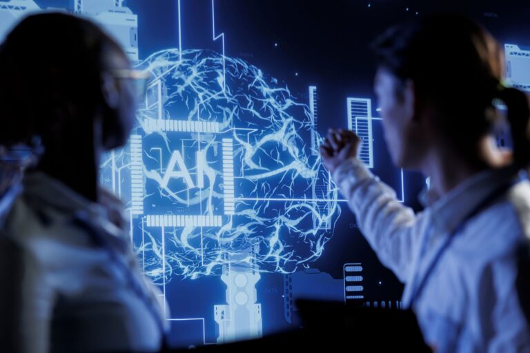 Two people look at a digital display of a brain with "AI" in the center, featuring circuits and technological elements in a blue color scheme.