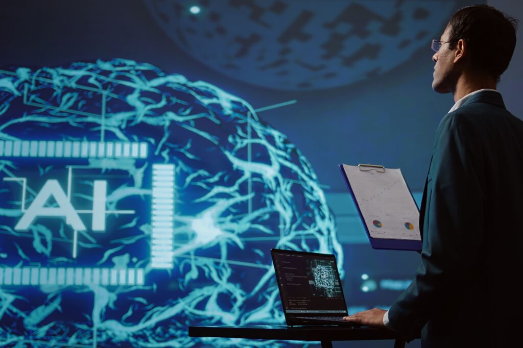 A person stands with a laptop and clipboard, facing a large digital screen displaying a brain graphic and the letters "AI," symbolizing AI business transformation and AI execution for SMEs.