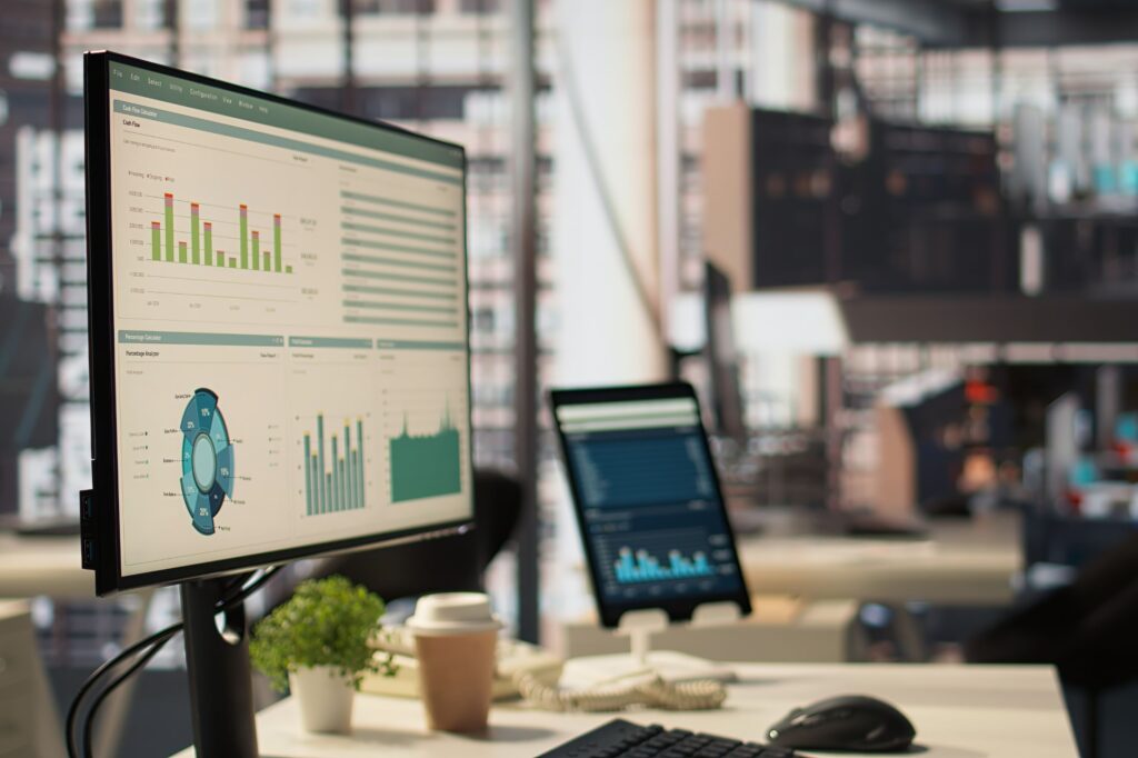 A computer monitor displays data charts and graphs in an office setting, highlighting how marketing automation tools for SMEs can streamline processes, with another laptop and office supplies visible on a desk in the background.