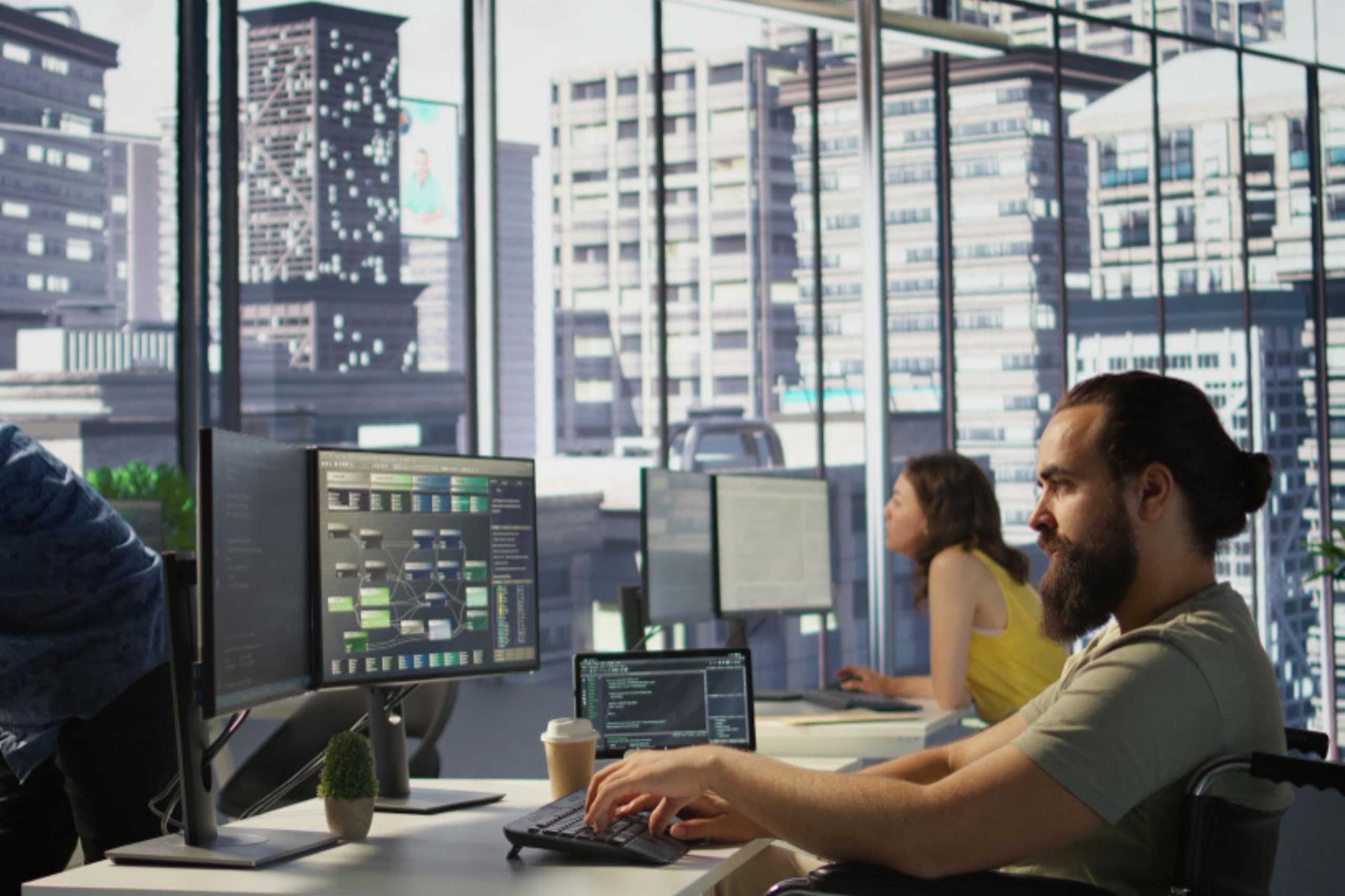 People working at computers in a modern office with large windows showing city buildings outside. Monitors display code and technical diagrams.