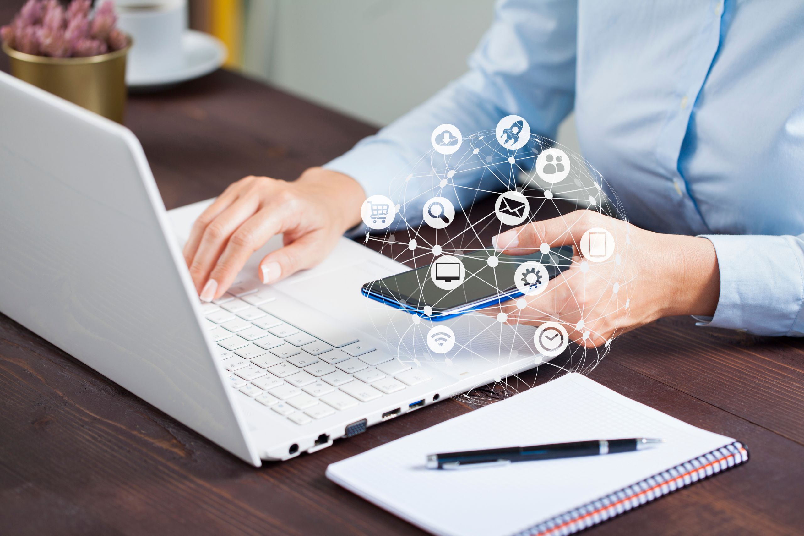 Person using a laptop and smartphone at a desk with digital icons representing various online services and applications overlaid near the devices, showcasing the importance of technology in supporting an effective Digital Transformation Strategy.