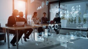 Four business professionals sit at a conference table with digital graphs and data visualizations displayed in the air, suggesting a discussion involving technology and analytics—an ideal scene for showcasing the impact of Fractional Technology Leadership or a Fractional CIO guiding strategic innovation.