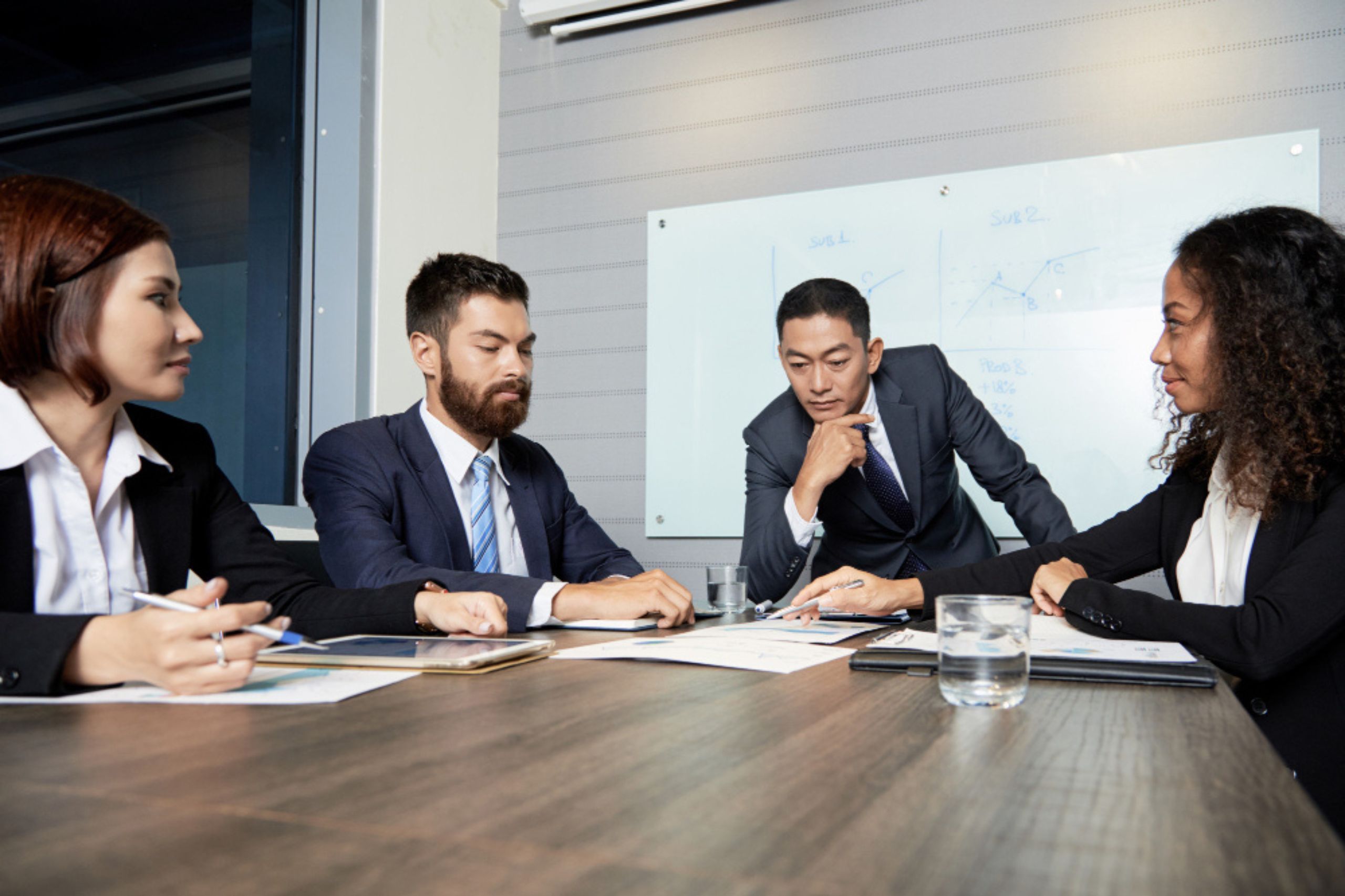 Four business professionals sit around a table with documents, engaged in discussion about their AI implementation strategy, with a whiteboard and graphs highlighting potential AI strategy mistakes in the background.